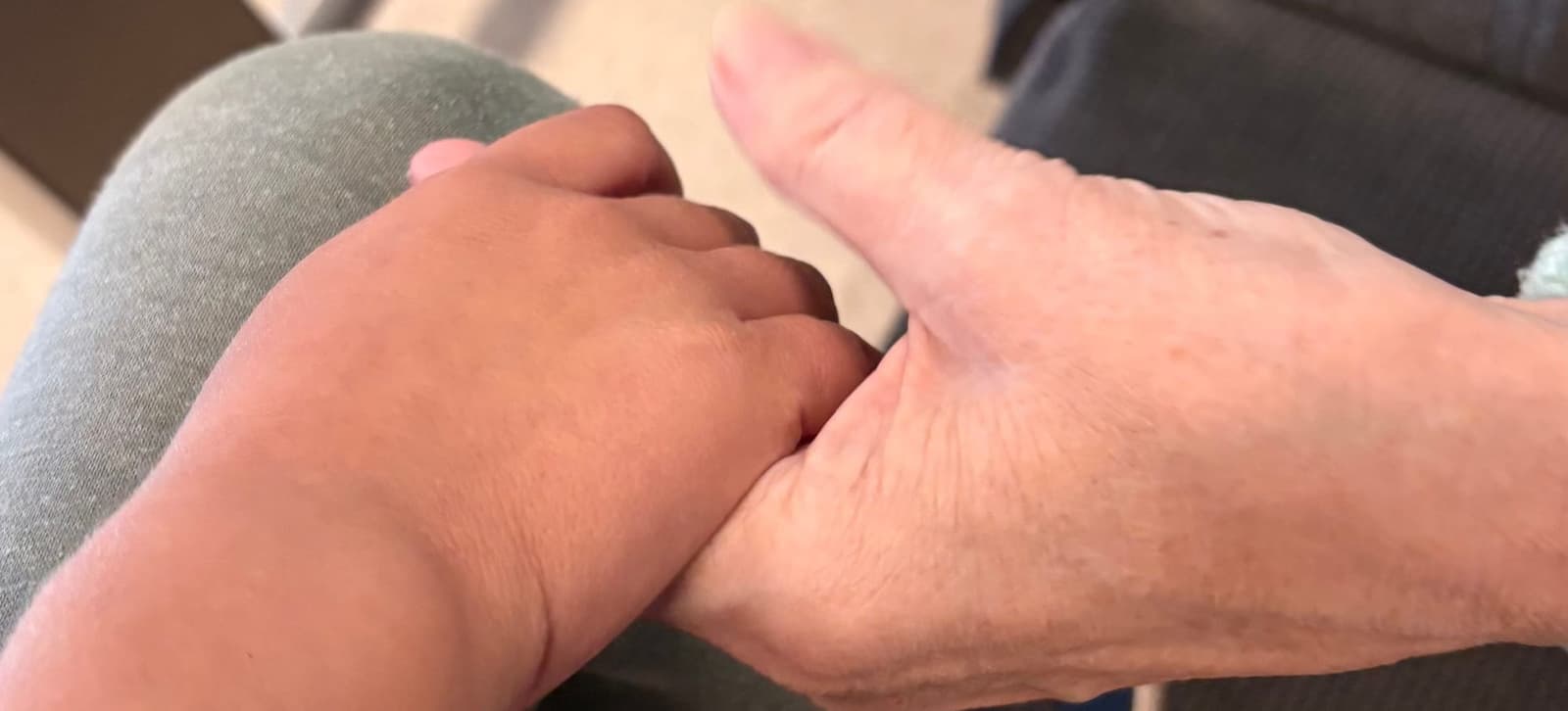 En liten barnehånd holder rundt tommelen på en eldre kvinnes hånd.