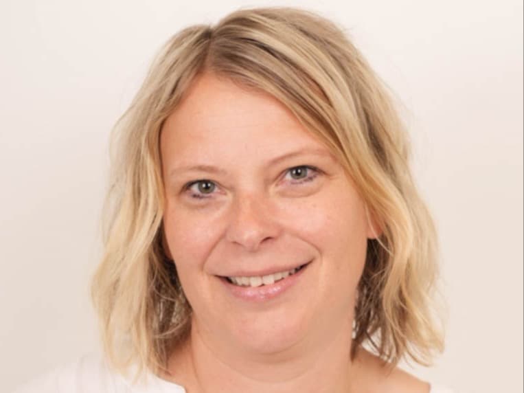 Hanne M. Nøding, portrett i hvit topp mot lys bakgrunn.